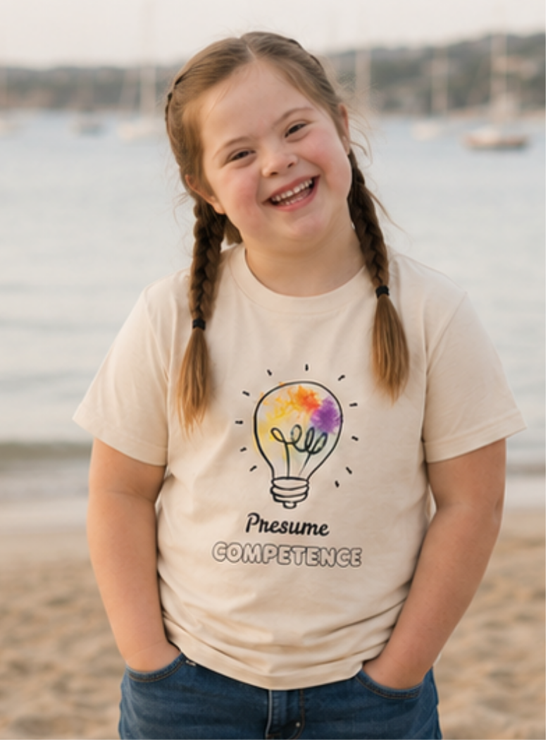 A smiling child wears Presume Competence T-shirt in a soft natural cream color, featuring a colorful lightbulb  illustration and the empowering message. Presume Competence. Set against a calm outdoor background, the image reflects confidence, kindness, and inclusion while celebrating the unique strengths of every child.
This meaningful graphic tee is designed for children of all abilities.
No collar tag, 100% cotton